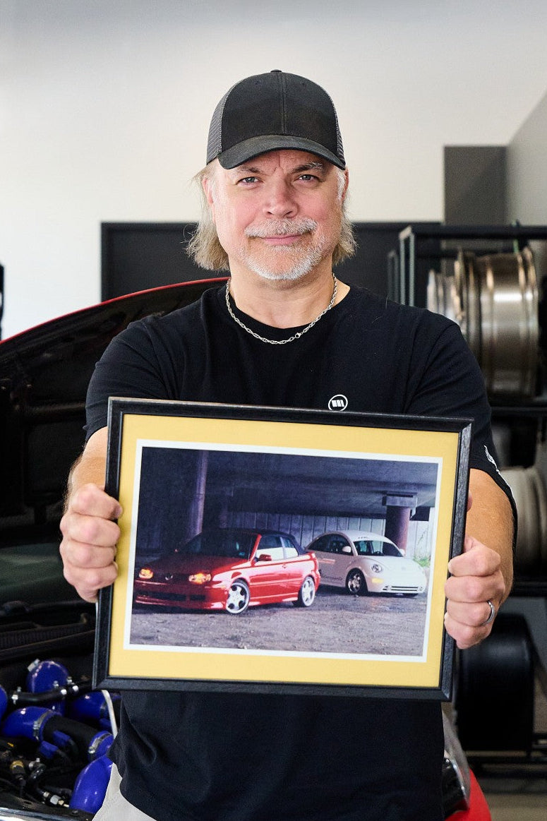 Man holding a framed picture of a red car in a garage setting